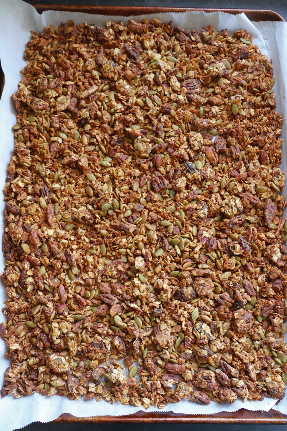 Homemade pumpkin spice granola with oats, pecans, and pumpkin seeds on a baking sheet.