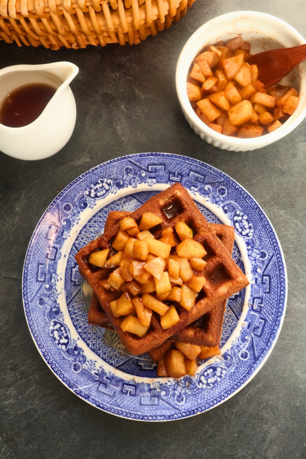 Stack of golden apple spice waffles topped with warm cinnamon-stewed apples and a drizzle of maple syrup.