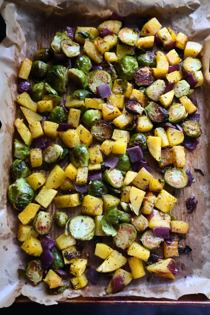 Sheet pan of harvest roasted vegetables with butternut squash, Brussels sprouts, and red onion.